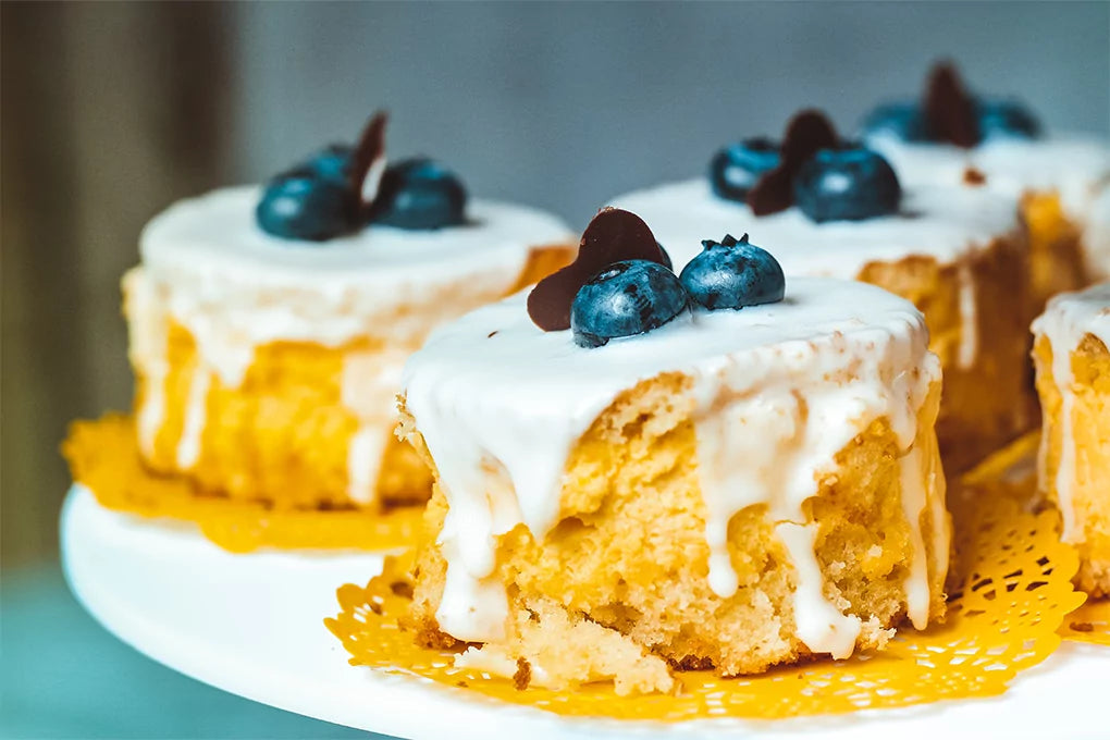Some delicious baked cake with white cream, fresh blueberries, and chocolate topping on it, placed on a pristine white surface