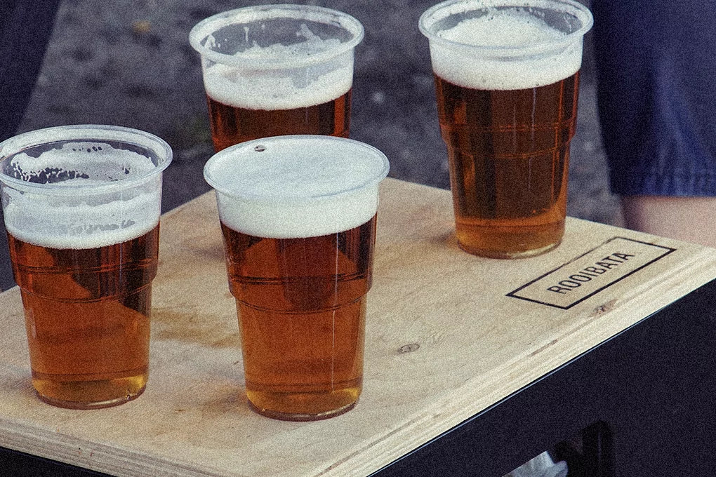A wooden tray is loaded up with four plastic cups filled with beer.