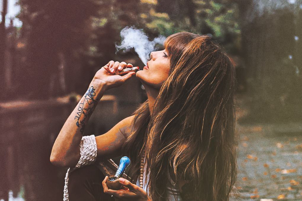 An image of a woman holding a joint in one hand and a smoke funnel in the other, exhaling smoke and visibly enjoying the moment