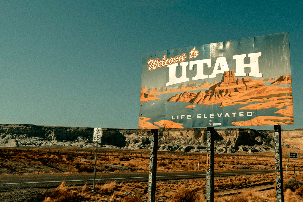 Scenic Utah landscape with blue skies, small mountains, and a welcoming sign that reads 'WELCOME TO UTAH'