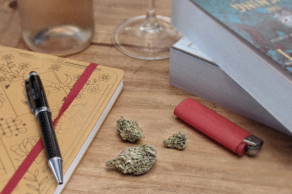 A few buds of CBD weed sit against a relaxing background of books, wine glasses and notebooks