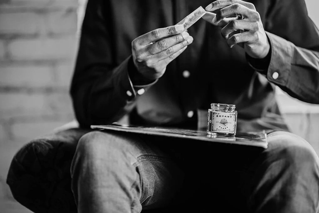 Someone rolls a joint on their lap from a jar of the best Sativa strain from Botany Farms.
