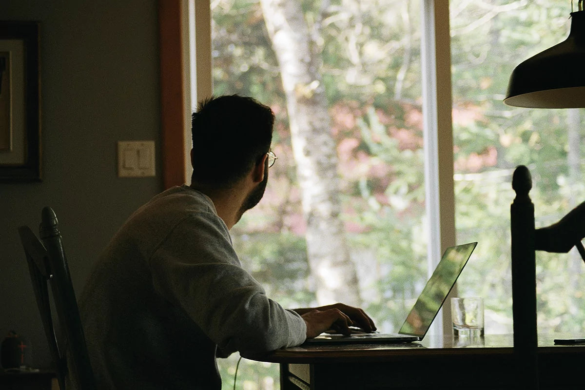 A man sits at a desk in front of his computer, but appears to be distracted as he's looking out the window.