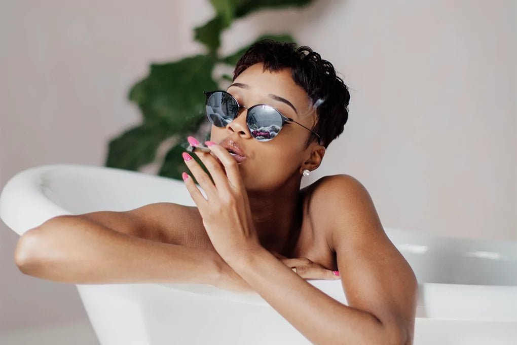 A woman rests on the side of a bathtub taking a puff of the best delta 8 weed strain for arousal.