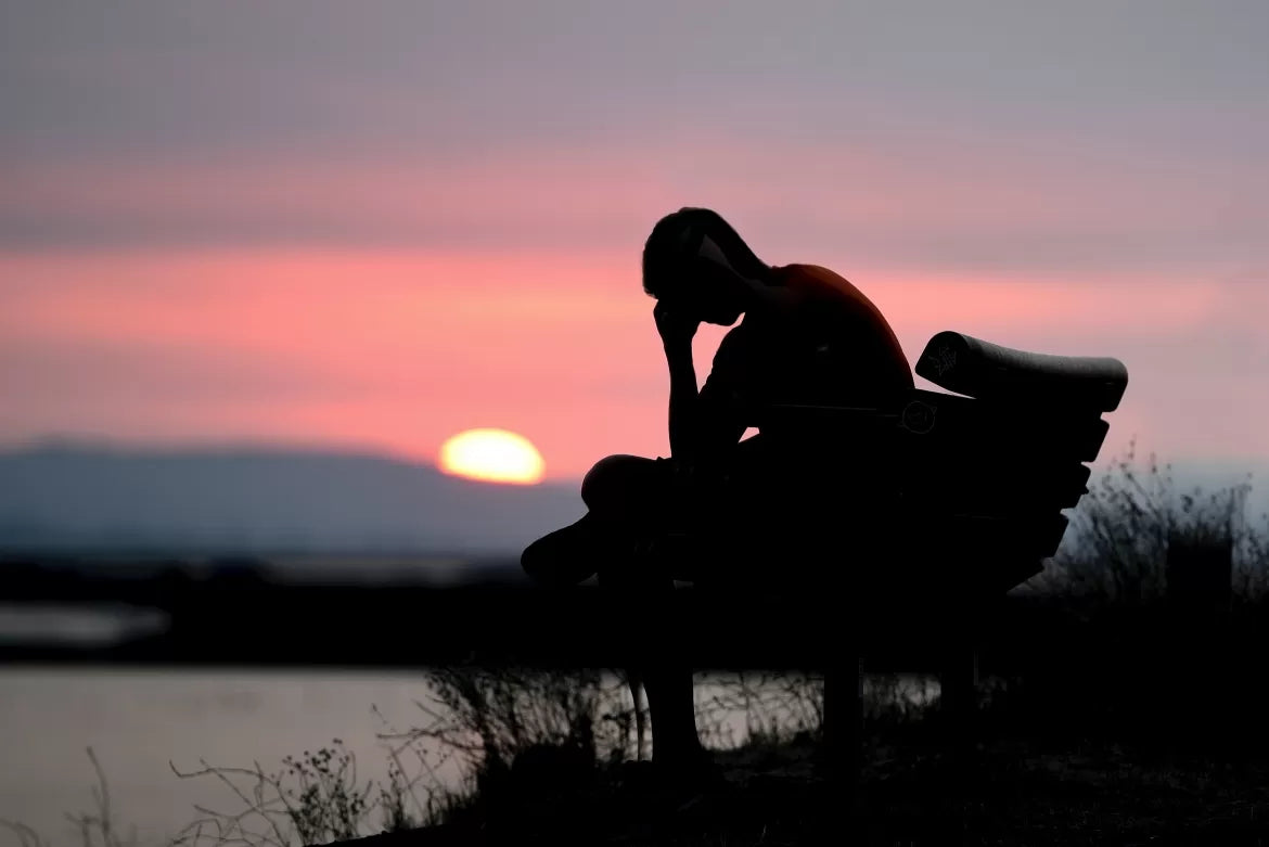 A depressed man sits on a bench in front of the water