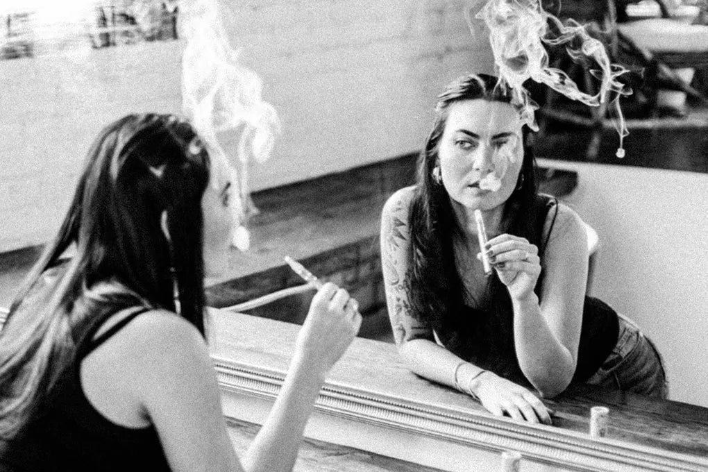 A black and white image of a woman looking at herself in the mirror while she smokes a vape packed with the best terpenes for anxiety