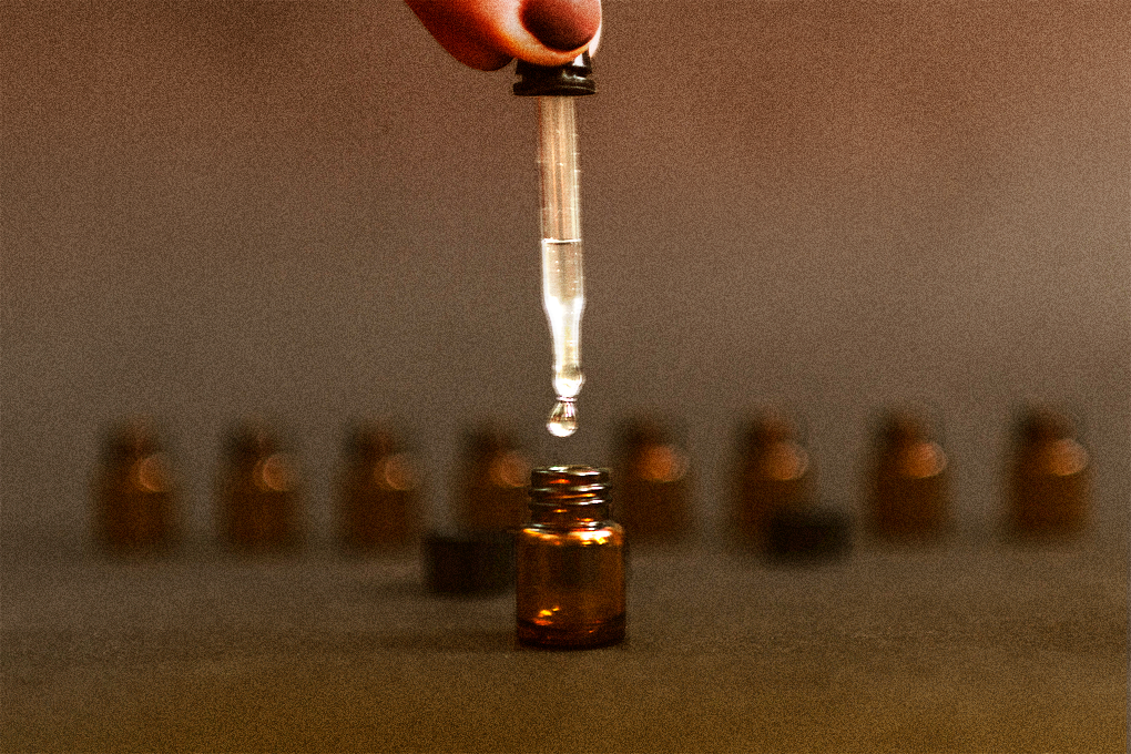 Two fingers holding a dropper to dispense liquid into a brown colored tincture with similar tinctures in the background