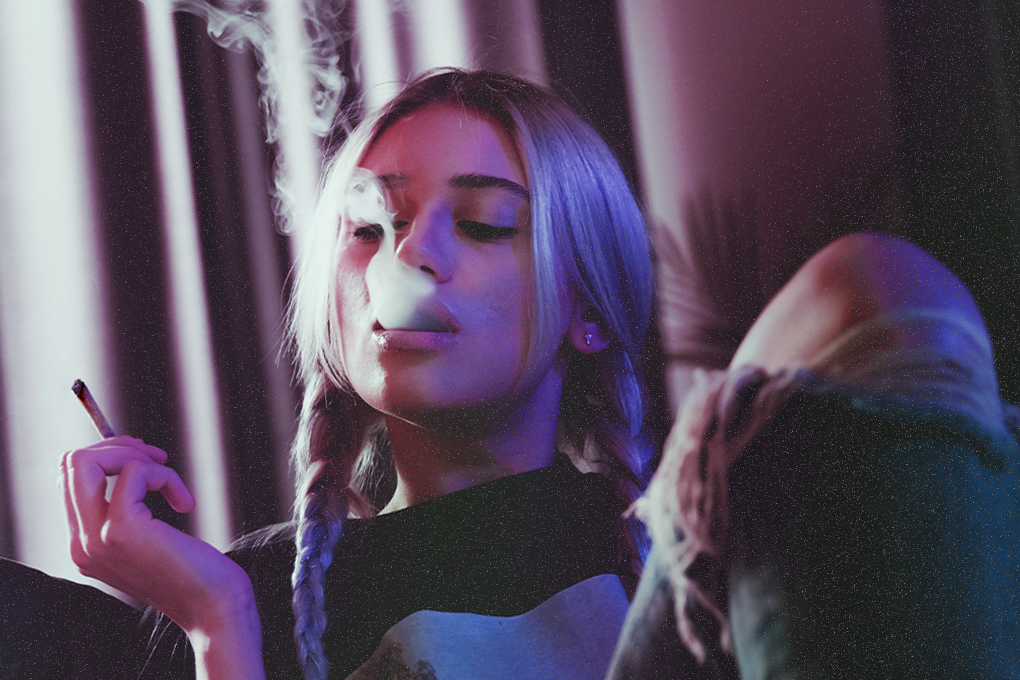 Woman enjoying a joint, exhaling smoke with closed eyes, experiencing relaxation and blissful moments