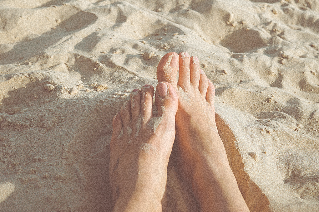 Two feet rest upon the sand in daylight