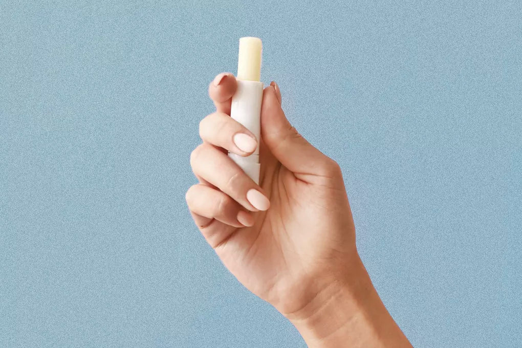A hand holds up a tube of CBD infused lip balm against a pastel blue backdrop.