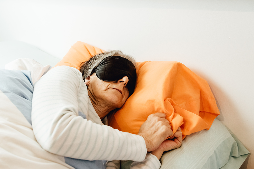Elderly woman peacefully sleeping on bed with sleep mask over her eyes in a cozy room