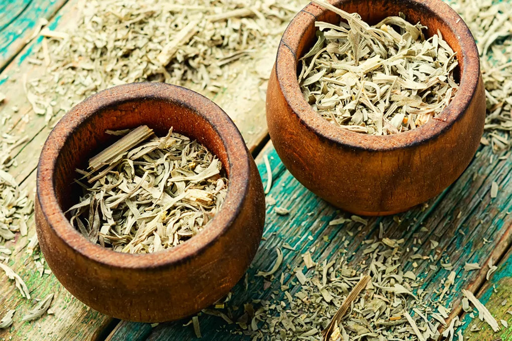 Two clay pots of dried Mugwort placed on a wooden bench that has dried Mugwort spread around