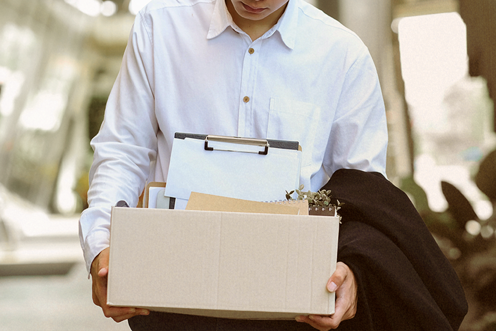 Sad man removing his jacket, holding a basket with official diary and files, symbolizing termination from the office