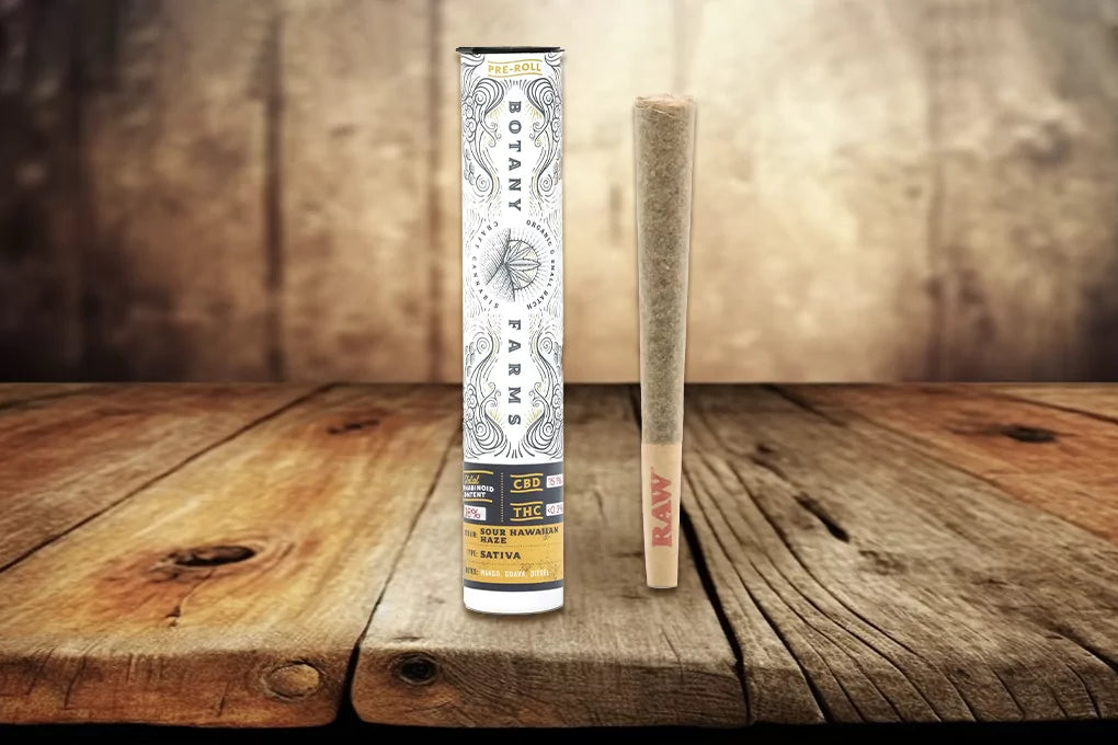 A Delta-8 pre-roll from Botany Farms stands upright on a wood surface next to a branded pre-roll tube.