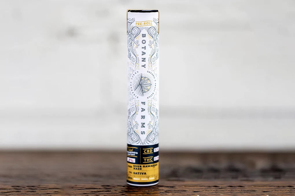 A tube of Botany Farms DElta-8 pre-rolls sits on a wooden table in the forefront against a blurry white background.