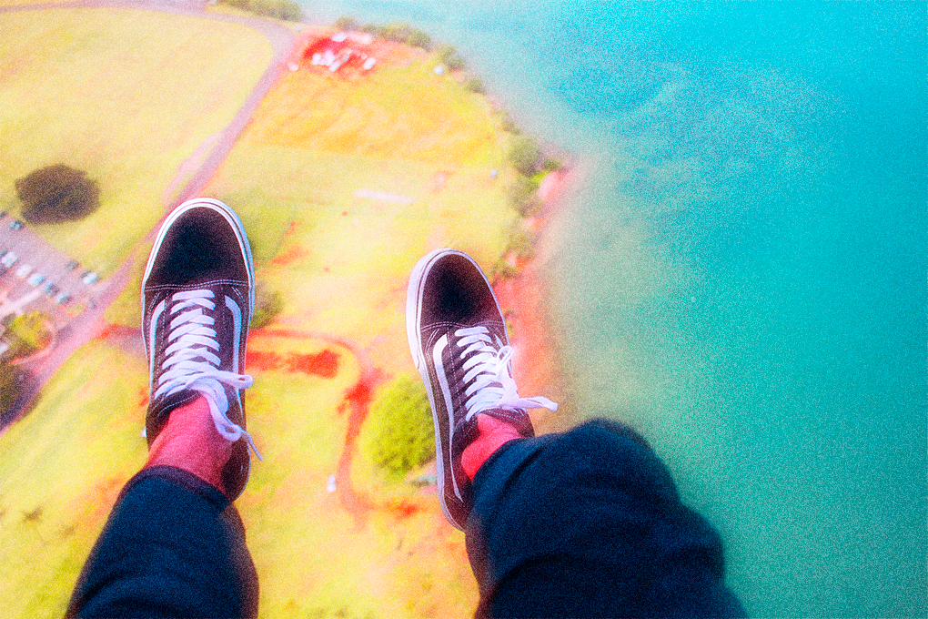 View from above of two legs hanging over scenic fields and sea below