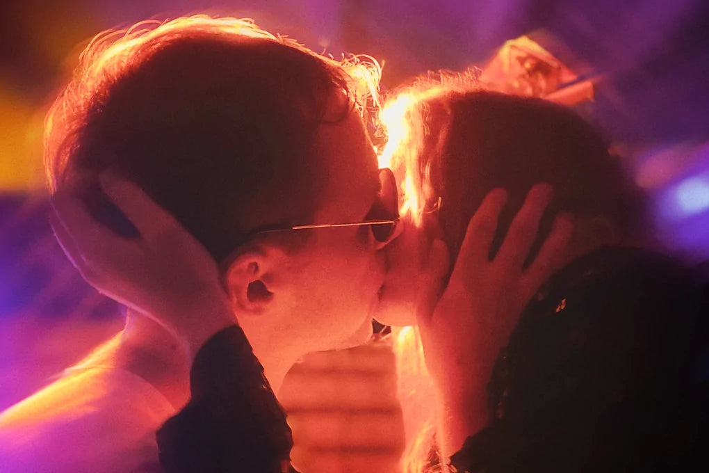 A couple kiss, holding each other as they are lit up in red.