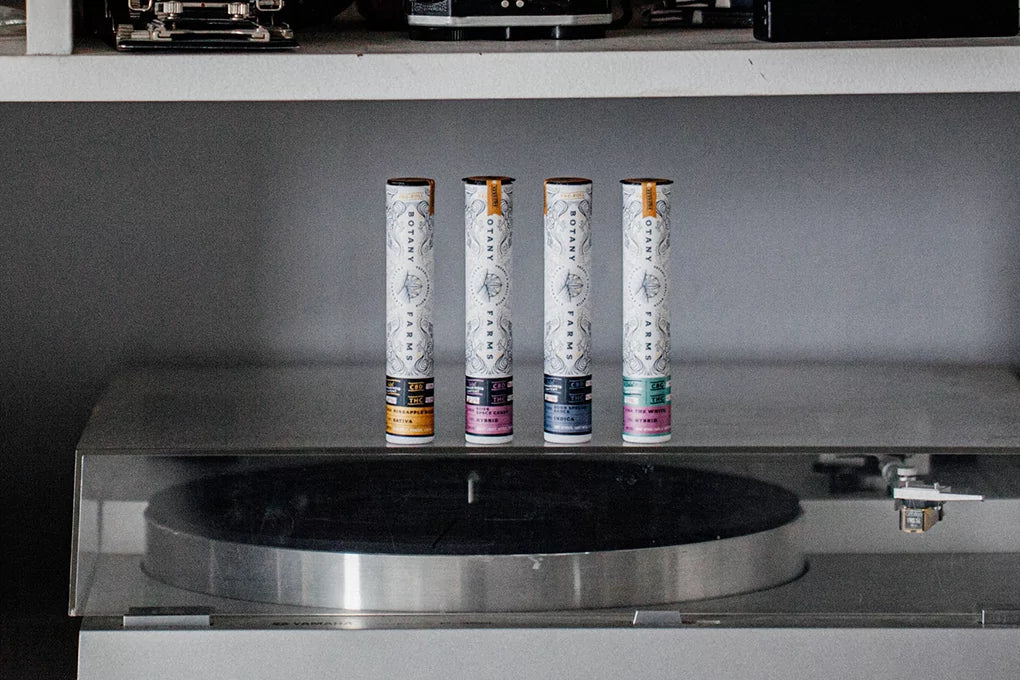 Four tubes of Botany Farms pre roll joints sit in a row on top of a record player.