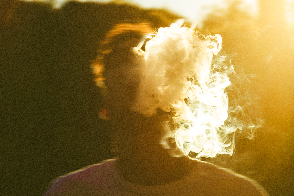 A boy looks up as smoke billows from his mouth, surrounded by a warm yellow glow