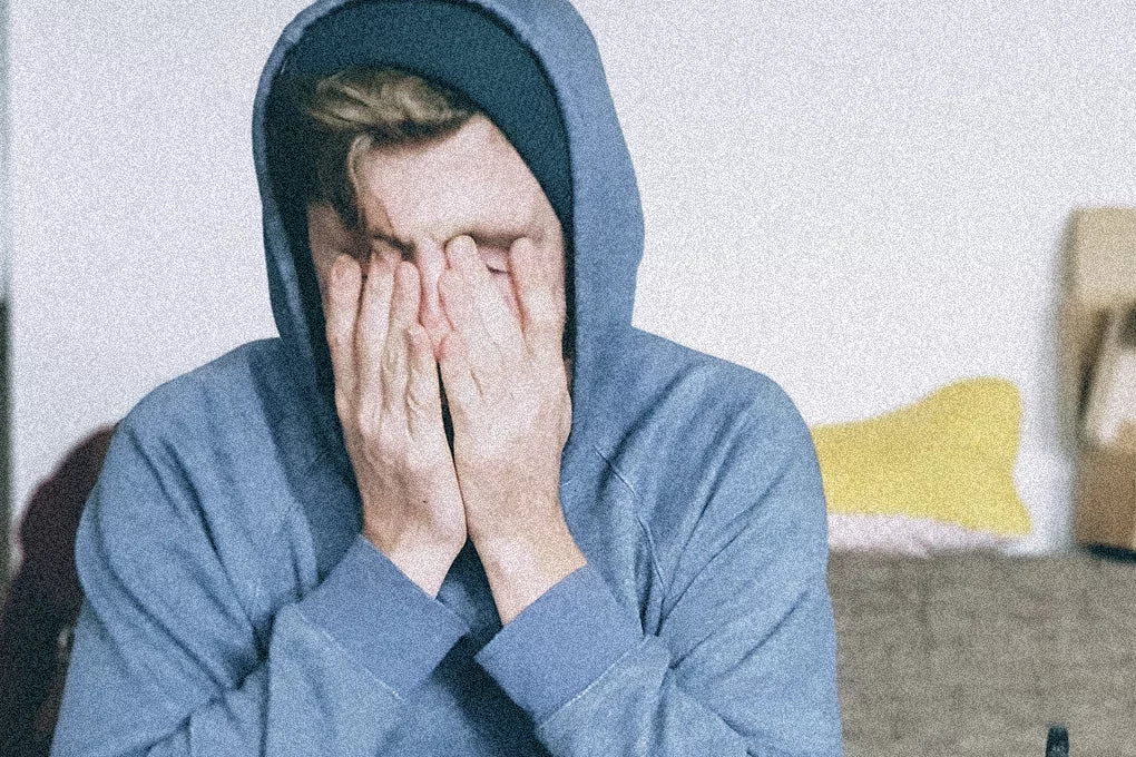 A person with a blue hoodie on holds their hands to their face rubbing their eyes.