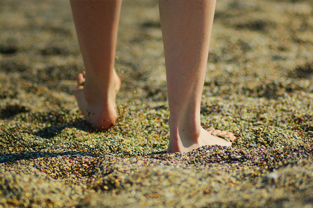 Someone standing barefoot on sunlit sand, feeling the warmth beneath their feet