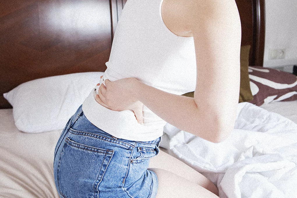 A person sits on a bed grabbing their lower back to relieve pain from inflammation.