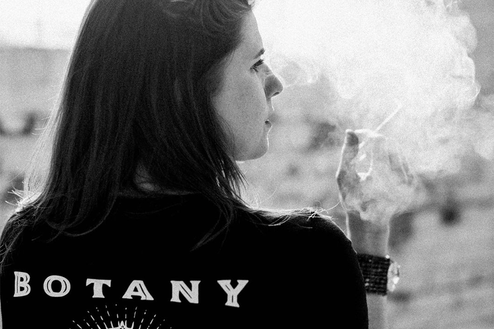 Back view of a woman smoking a marijuana joint with a 'BOTANY' print on the back of her shirt