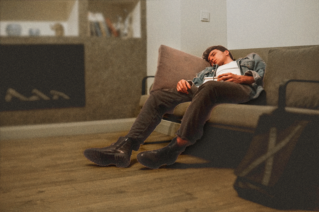 A man peacefully asleep on a sofa, dressed in a jacket, pants, and shoes, in a room