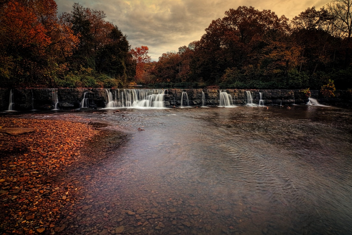 A beautiful water fall in Arkansas is surrounded by a red and orange forest in autumn