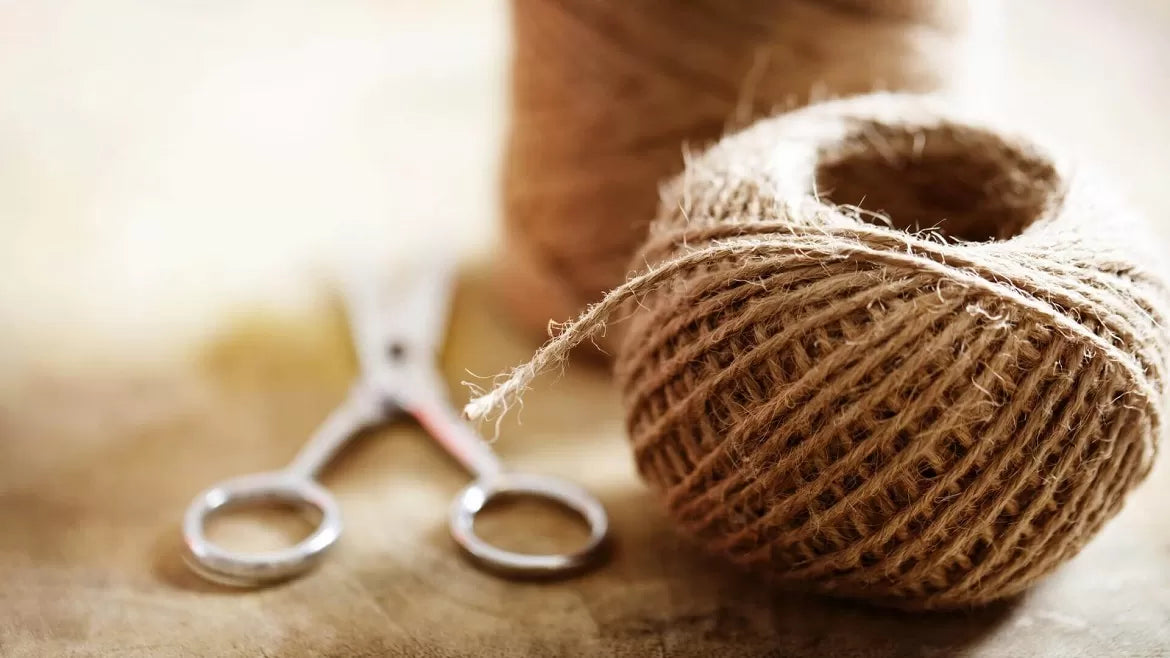 A hemp wick roll is next to a pair of scissors on top of a table.