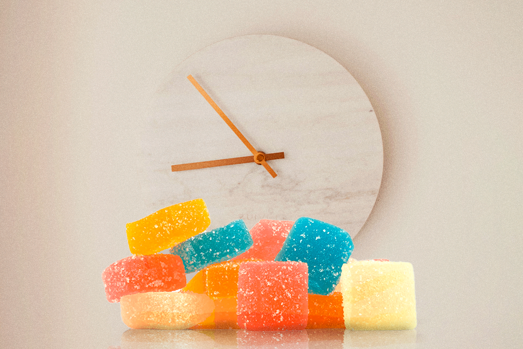 Assorted colorful gummies on a white surface, with a clock in the white background