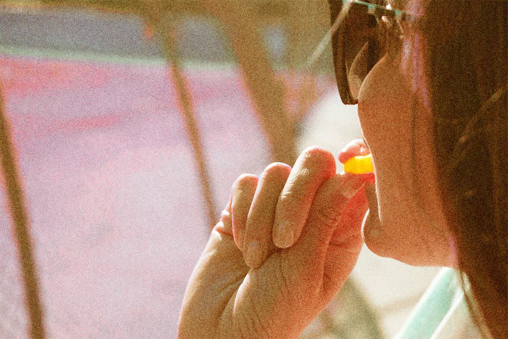 A woman wearing a sunglass holding a delta 10 gummy up to her mouth