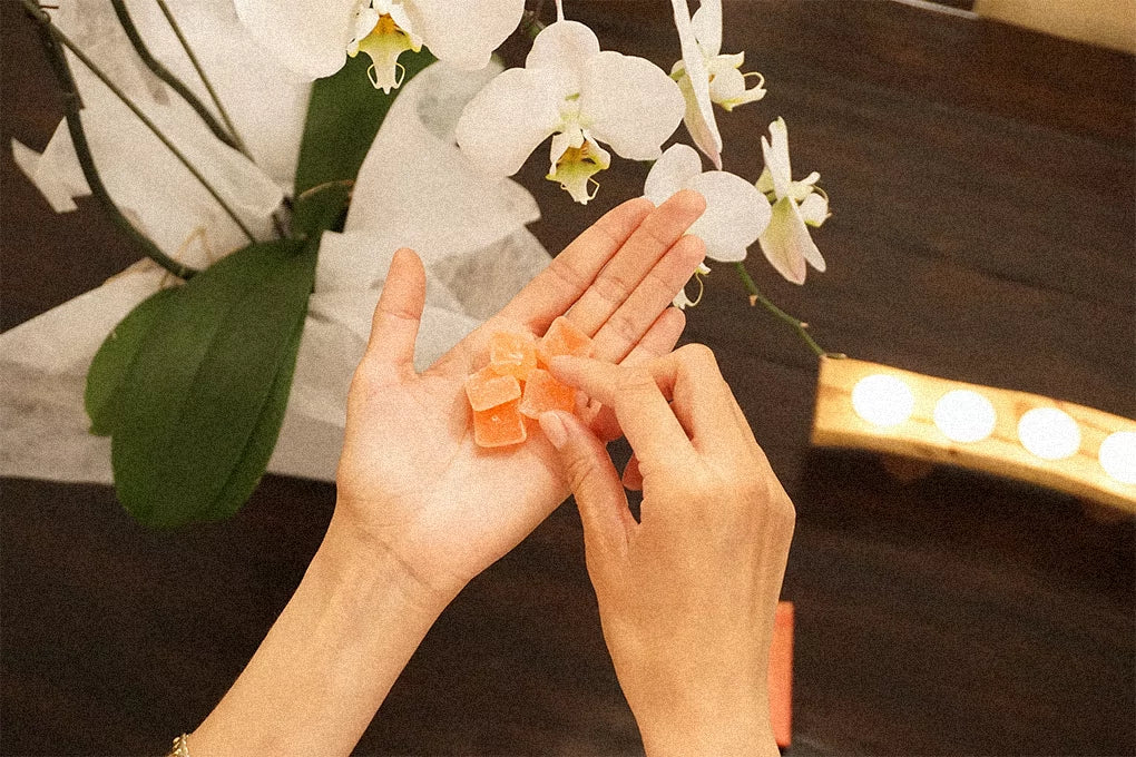 A shot of someone's hands, holding orange Delta-8 gummies in the palm of one hand and picking one up with the other.