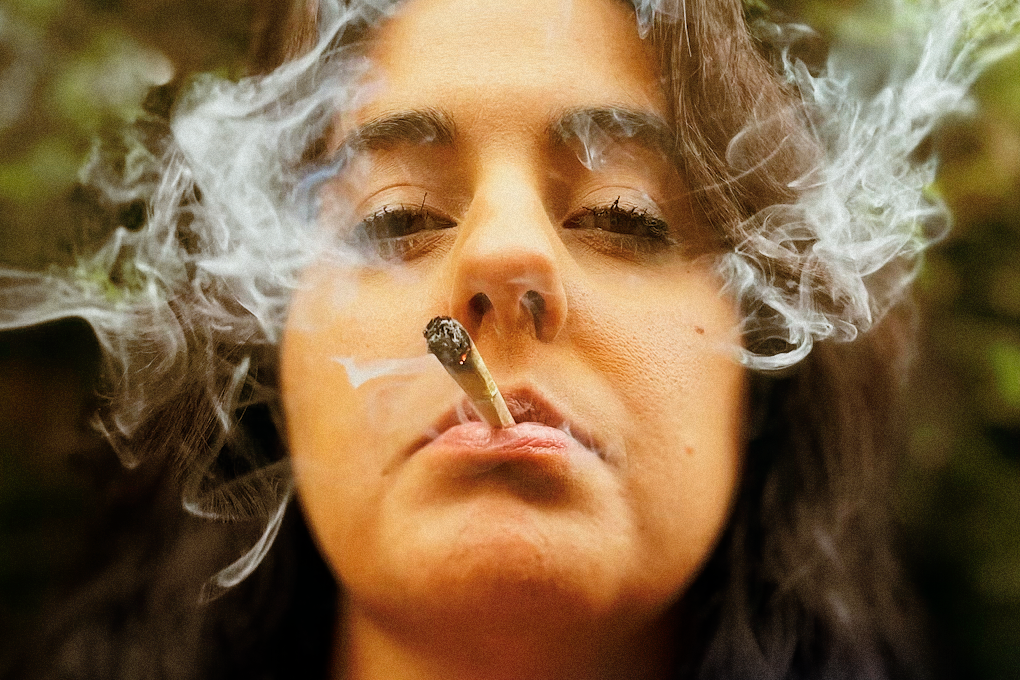 A woman smoking a joint and exhaling smoke in a relaxed manner.