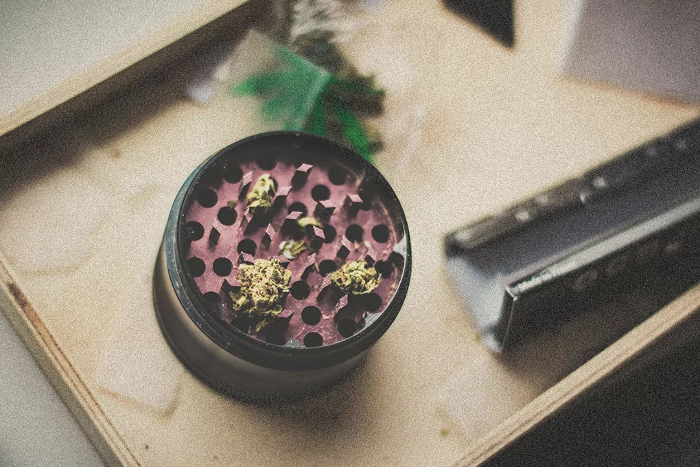A purple weed grinder filled with a little bit of weed sits next to rolling papers on a table
