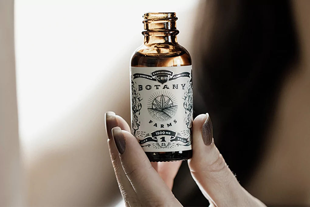 A hand holds up a bottle of CBD oil used to make CBD oral spray