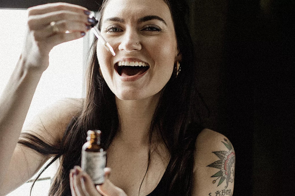A woman holds up a vial and dropper filled with CBD tincture