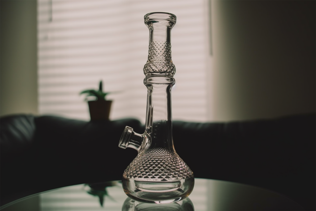 A glass bong, with the stem removed, sits on a table against a blurry living room background.