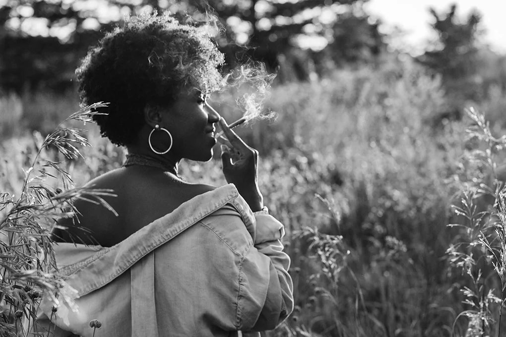 A woman smokes cannabis in a grassy field wondering how to prevent red eyes from marijuana