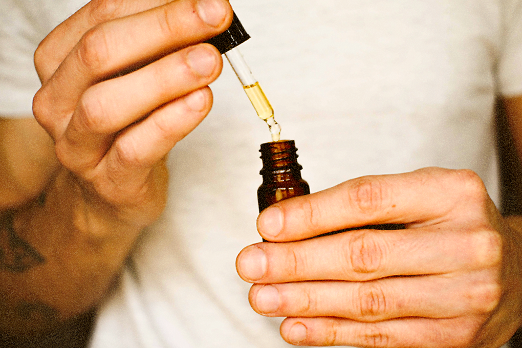 A man is holding a tincture in his left hand and a dropper in his right hand, with some liquid present in the dropper