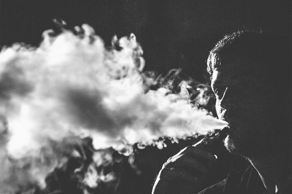 A silhouette of a man blowing out smoke from a CBD vape.