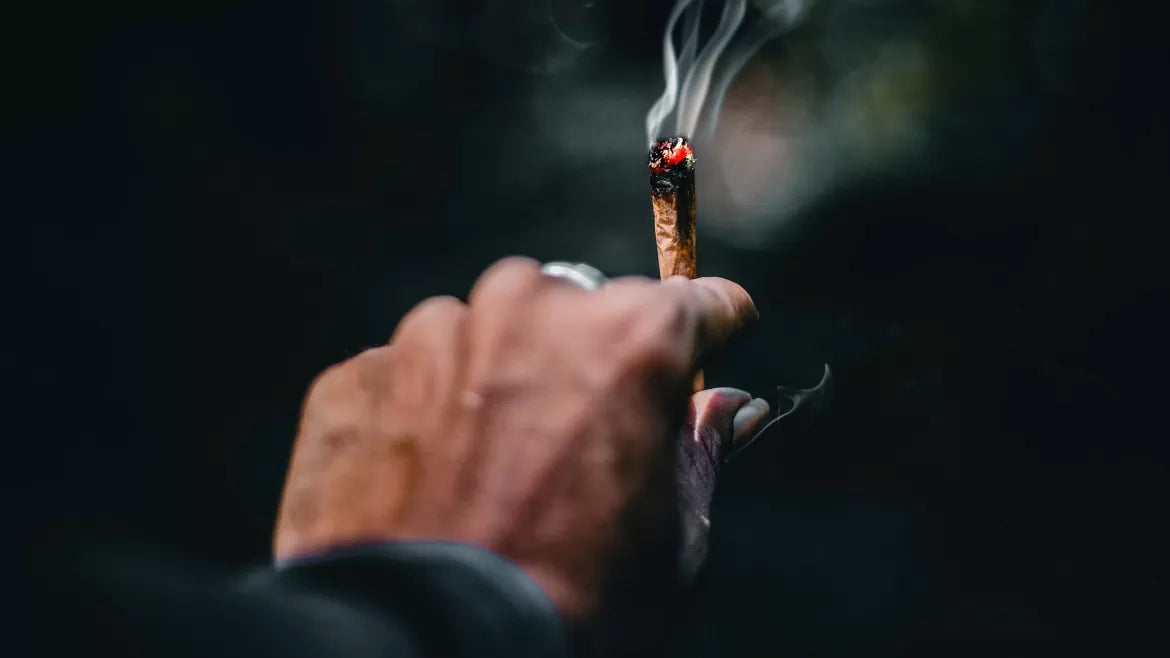 A man holds a perfectly lit joint after showing his friend how to light a joint