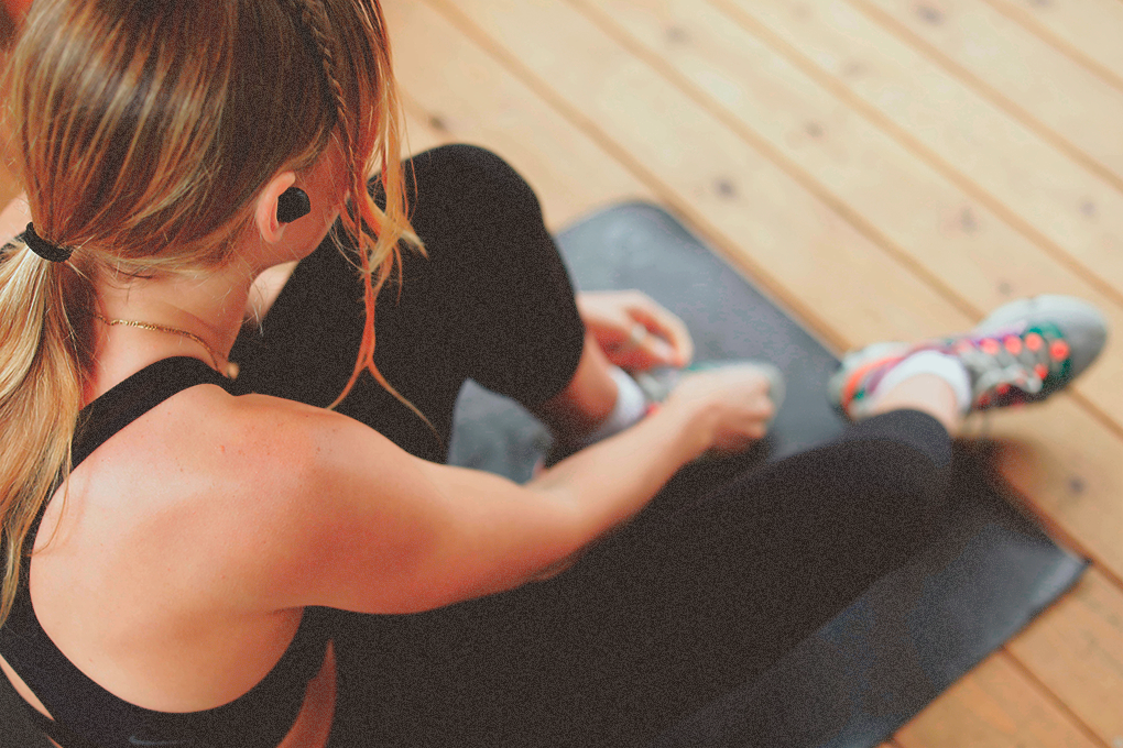 Woman in tracksuit tying shoelace, gearing up with earphones for a workout session on the floor