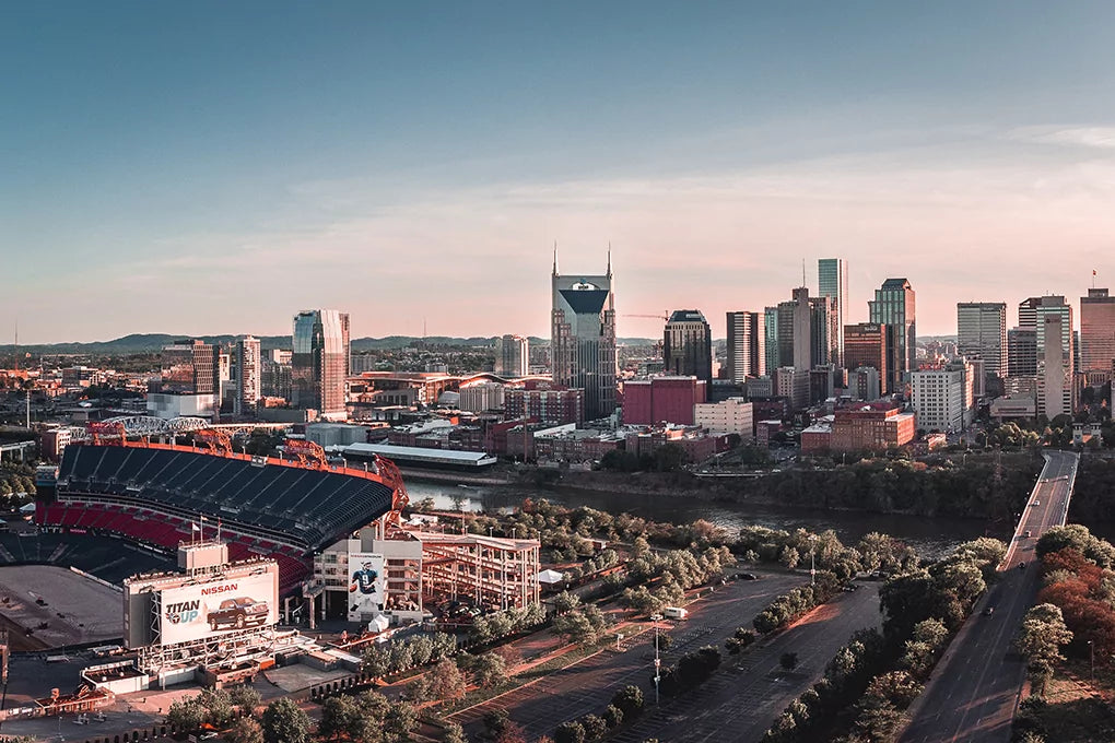 The vibrant cityscape of Nashville, Tennessee in daylight, featuring buildings big and small, a stadium, roads, and a flowing river
