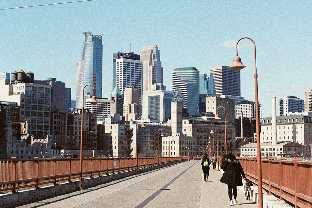 Front view of the Stone Arch Bridge in Minnesota, with people walking across it and buildings surrounding the area