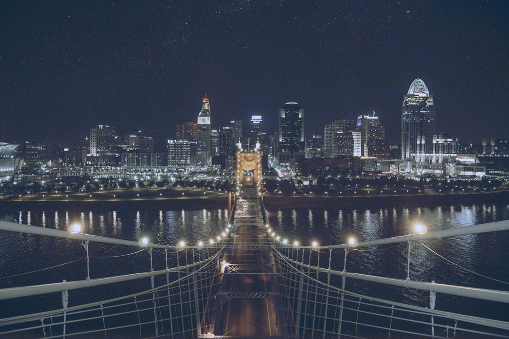 Nighttime glow on John A. Roebling Suspension Bridge in Ohio, with lights illuminating the bridge and riverside buildings