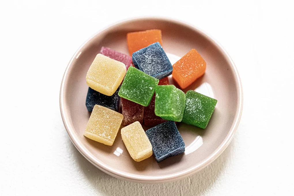A bowl of colorful THC gummies sits on a white table