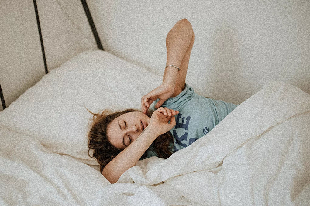 A photo a a woman in bed stretching her arms out after sleep.