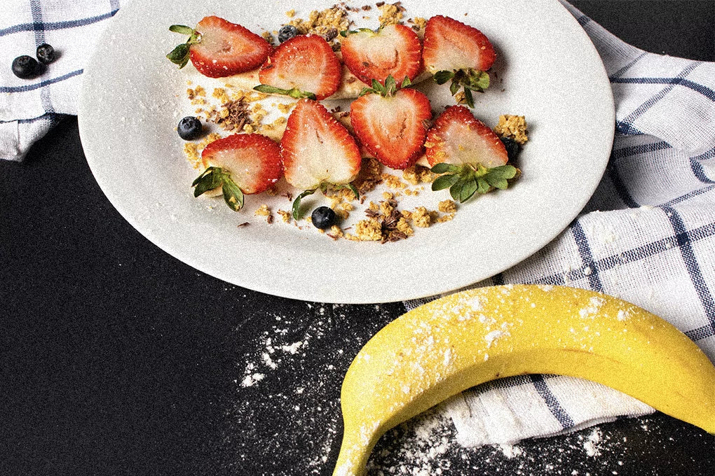 A white bowl of strawberry cereal sits on a table next to a banana.