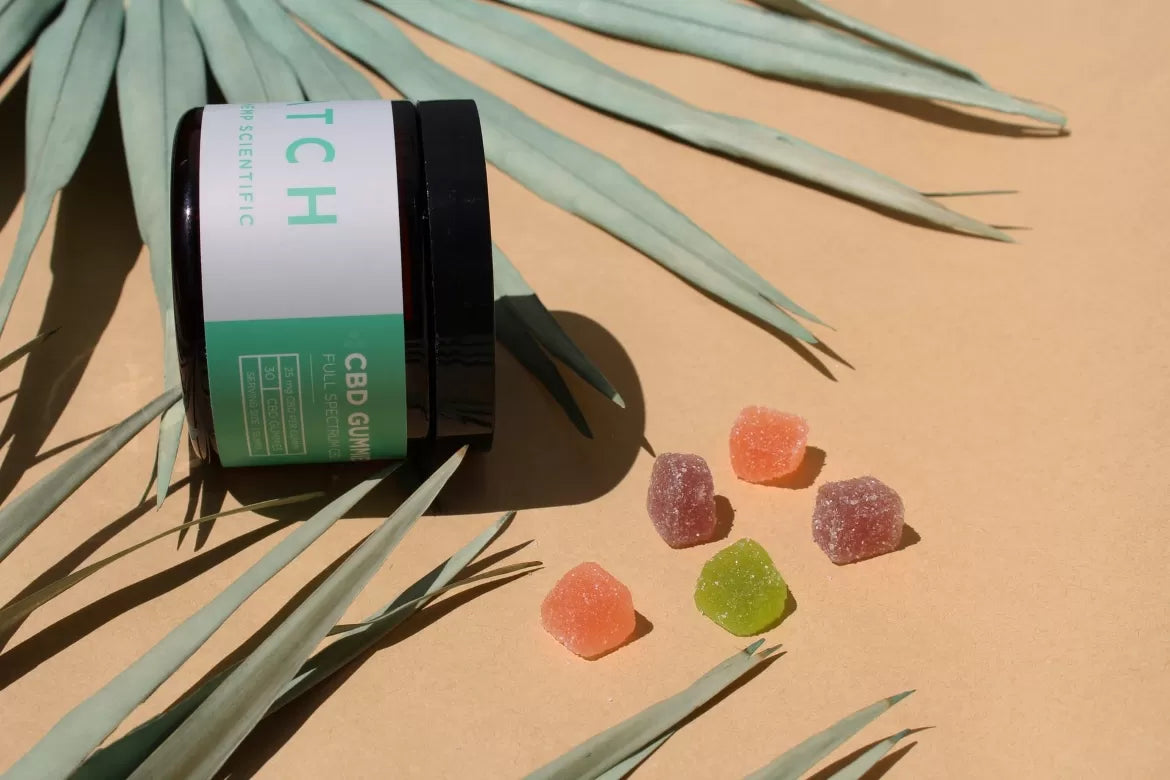 CBD gummies spill out of their container onto a tan background